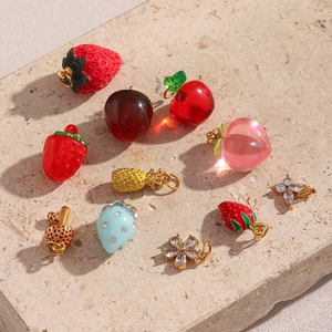 Détail de breloques dorées 18K aux formes de fruits et fleurs posées sur pierre texturée