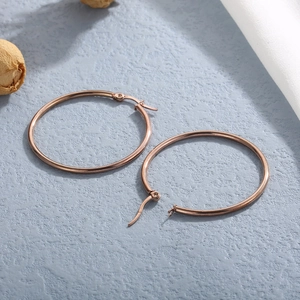Detail view of round rose gold stainless steel hoop earrings on blue textured background
