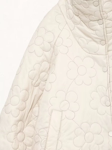 Detail of floral quilted texture and matching snap buttons on a cream puffer jacket