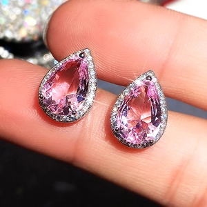 Pear-cut pink zircon stud earrings in silver setting held between fingers