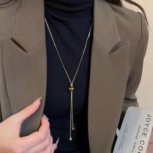 Detailed view of a gold snake chain necklace with a tiger eye sphere and long tassel