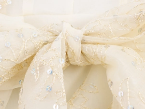 Détail macro d'un nœud en organza avec broderie dorée et sequins sur la robe élégante