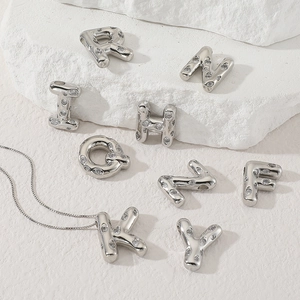 Silver alphabet letter pendants with micro-set zircons and thin chain on white stone