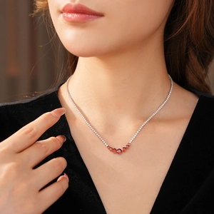 Detail of silver necklace featuring a curved red zircon pendant worn on a model