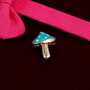 Macro detail of a small blue mushroom charm with white dots on red velvet fabric