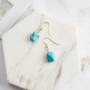 Macro view of blue turquoise drop earrings with gold hooks on marble background