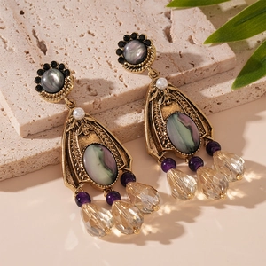 Vintage gold drop earrings with purple beads and clear crystal pendants on a stone background