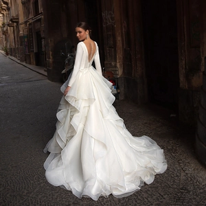 Elegant white long sleeve bridal gown with deep V-back, layered ruffles and long train