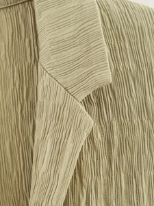 Macro shot of olive green textured fabric with fine pleated details and neckline finish