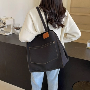 Detail of black canvas tote bag with contrast yellow stitching and brown leather patch