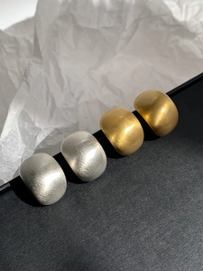 Detail of minimalist geometric brushed texture earrings in gold and silver metal finishes