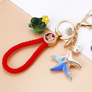 Starfish shell pearl keychain with red leather rope and gold lucky charm on wood background
