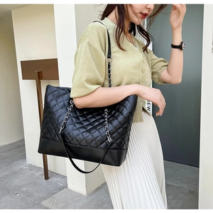 Close-up detail of quilted black tote bag with metallic chain and leather strap on shoulder