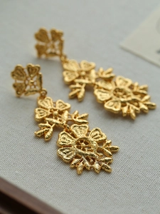 Macro view of gold flower drop earrings with intricate embroidery metal texture on white linen