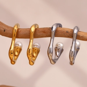 Detailed view of minimalist gold and silver C-shape metal earrings with pearls on wood