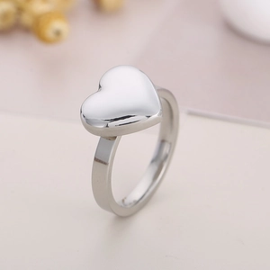 Close-up of minimalist silver heart ring with polished finish on a soft pastel background