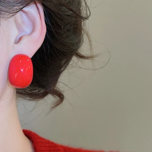 Close-up of a model wearing smooth red teardrop earrings with a glossy finish