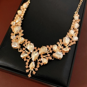Detail of elegant gold drop-shaped crystal necklace set on black jewelry display stand
