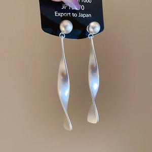 Détail de boucles d'oreilles pendantes torsadées en métal mat au design géométrique