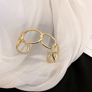Close-up of gold chunky chain link open bangle displayed on elegant white fabric drapery