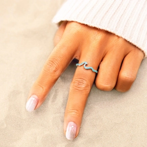 Close-up of S925 sterling silver wave ring with blue zircon inlay on sand background