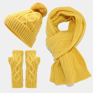 Close-up of yellow cable knit winter set including beanie with pom-pom, scarf and gloves