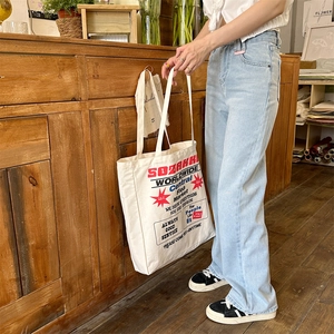 Close-up of a white canvas tote bag with retro SOZAKKI print and long shoulder straps