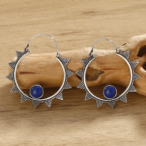 Detailed view of silver hoop earrings with solar patterns and blue gemstone on wood
