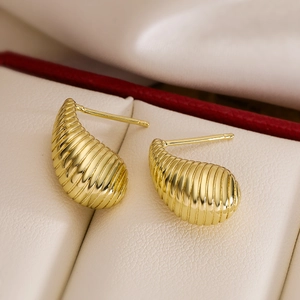 Golden teardrop stud earrings with ribbed metal texture on a silk and leather display