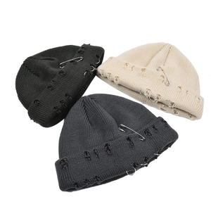 Detail of distressed knit beanies with metal safety pins and ring accessories in three colors