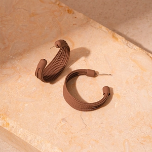 Detail of brown C-shaped earrings with ribbed texture on a natural stone surface
