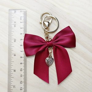 Deep red satin bow keychain with silver heart pendant and gold clasp on wood background