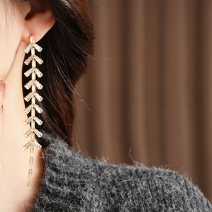 Macro view of gold leaf tassel earrings with clear crystals worn on a female model