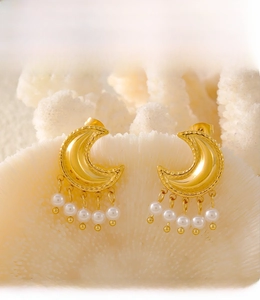 Detail of PVD plated gold moon earrings with faux pearl tassels on white coral