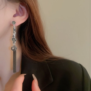 Detail of long fringe earrings with dark stones worn by a model in a black suit