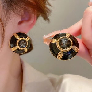 Detailed close-up of vintage gold metal earrings with black enamel and a faceted gemstone