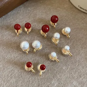 Elegant gold pearl clip earrings set in red and white on a soft textured surface