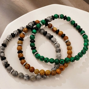 Three natural stone beaded bracelets with malachite and jasper on a white display tray