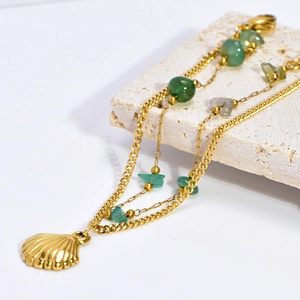 Detail of double-layer gold anklet with green natural stones and a gold shell pendant