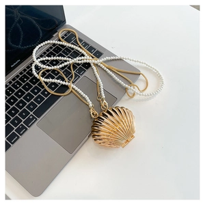 Macro shot of gold shell-shaped evening bag with pearl handle and metal chain on desk