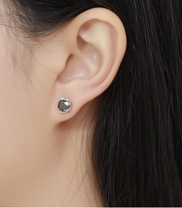 Close-up of a model wearing a black faceted stud earring set in silver plating