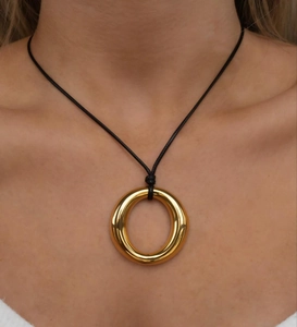 Close-up of model wearing a chunky gold circle pendant on a black wax rope necklace