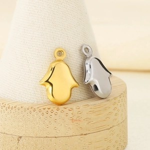 Gold and silver stainless steel Hamsa hand charms on a minimalist wooden display stand