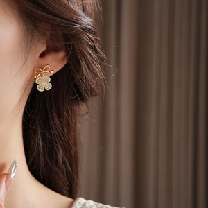 Detail showing shell flower earrings with golden bow and pearl worn by a model