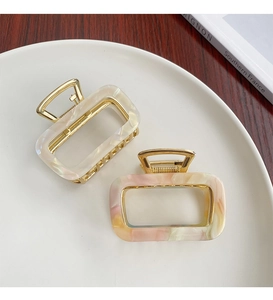 Detailed shot of two marble acetate hair claws in white and pink-yellow on a tray