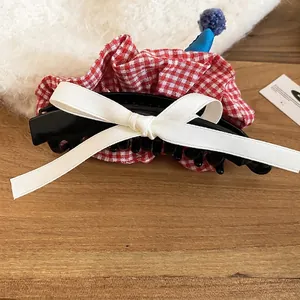 Cute bow hair clip with red gingham pattern and white silk ribbon on a wooden background
