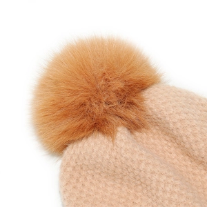 Close-up of beige knitted beanie texture with a large fluffy orange pom-pom top