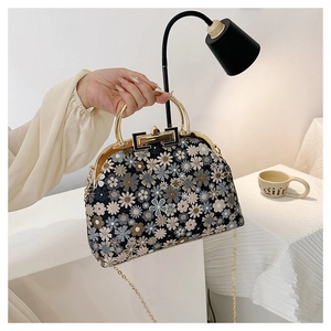 Detail of hand-held black bag with floral embroidery and golden metal round handle
