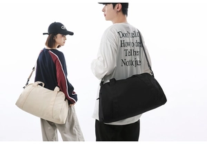 Lifestyle view of models carrying large capacity travel duffel bags in black and beige