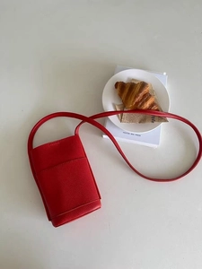 Close-up of red lychee textured mini crossbody bag on a white table with a magazine